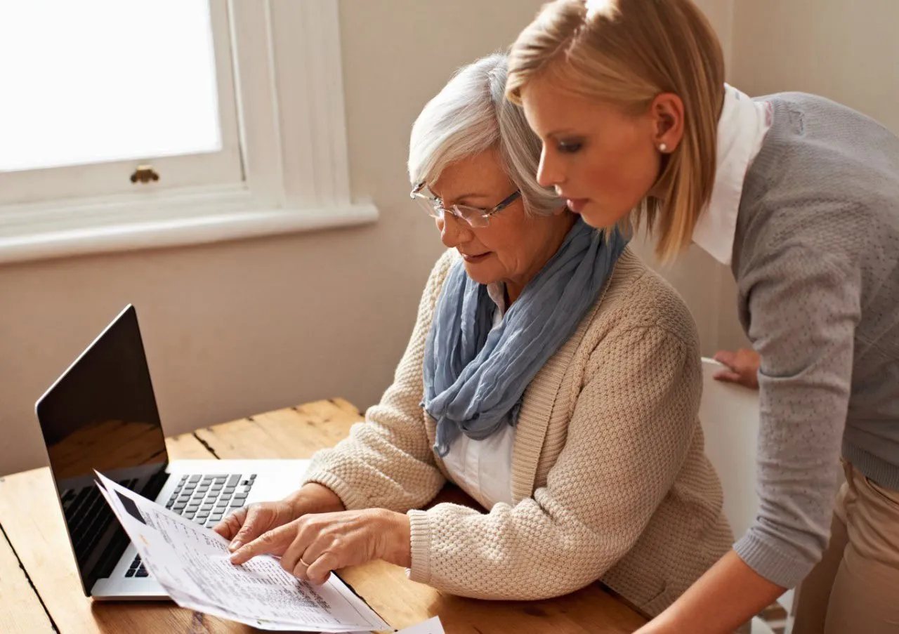 An advisor helping an older woman review documents at a laptop