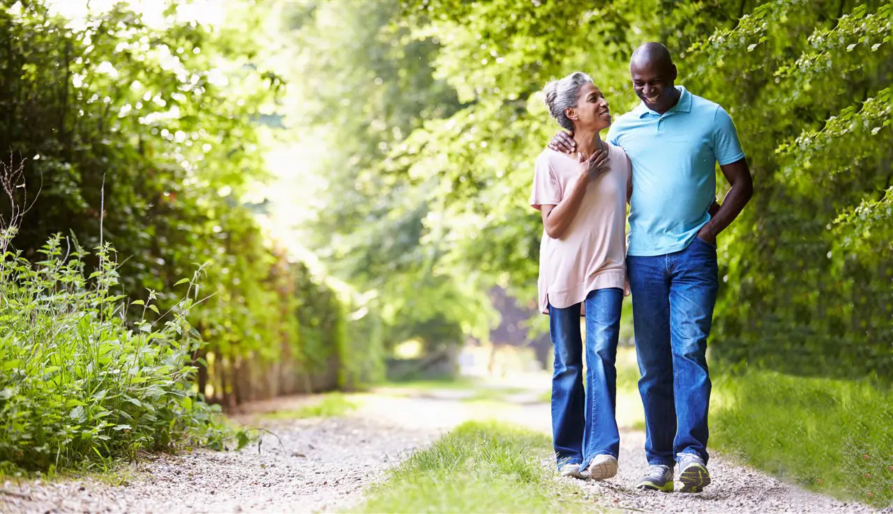 An older couple walking together on a tree-lined path