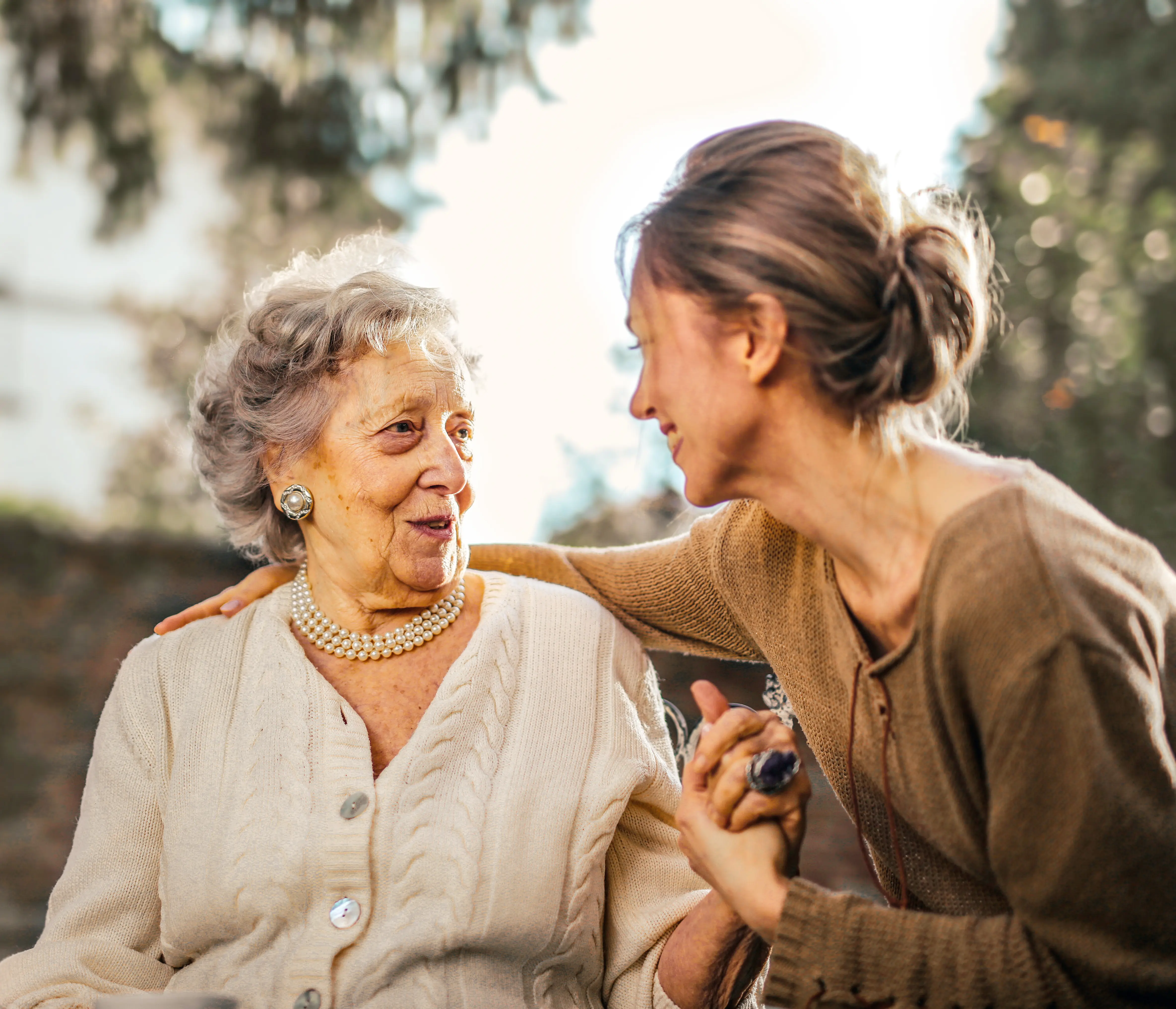 A caregiver tenderly holding hands with an elderly woman outdoors